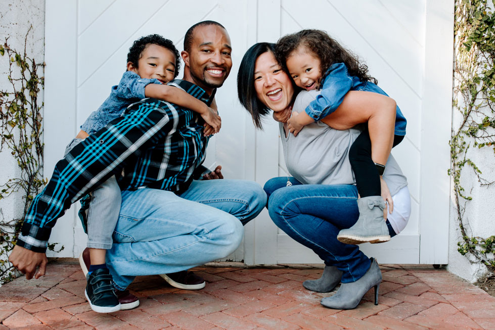Asian mother and Black dad on brick porch with smiling mixed race children.